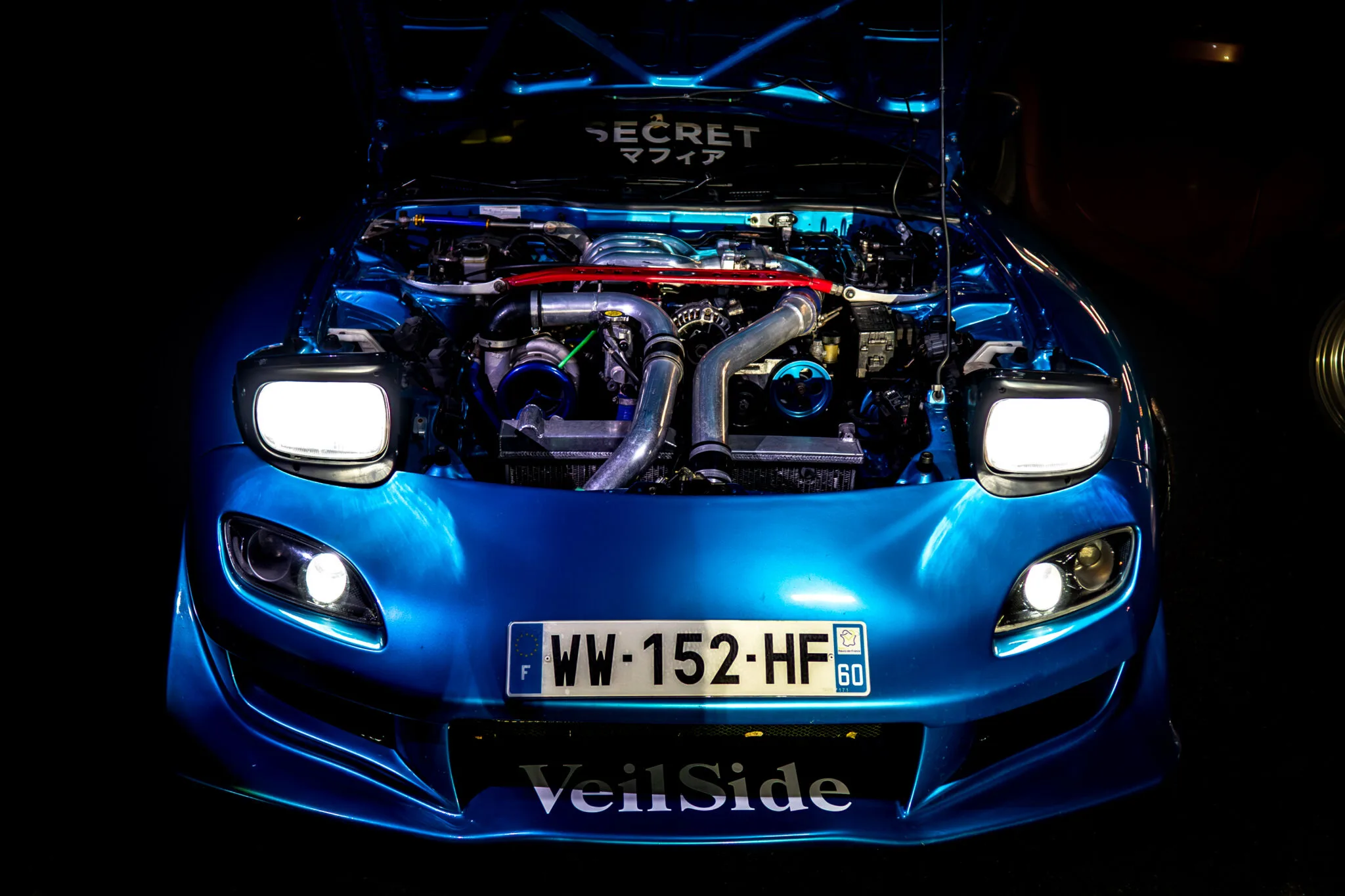 Mazda RX-7 bleue, capot ouvert et phares allumés dans la nuit